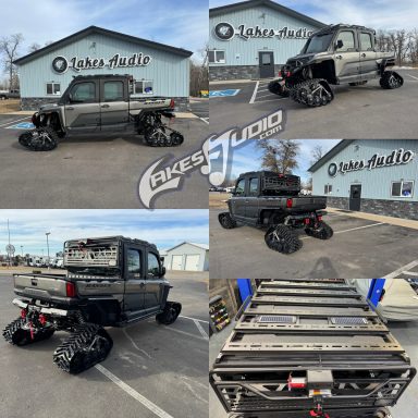 Black pickup truck with unique large wheels, parked outside a building with a sign.