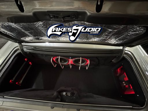 Car trunk with custom audio setup, illuminated with red lights and featuring a brand logo.