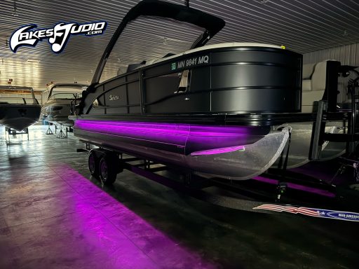 A sleek black pontoon boat with purple LED lighting in a showroom.