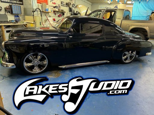 A classic black car with custom wheels, displayed in a garage setting.